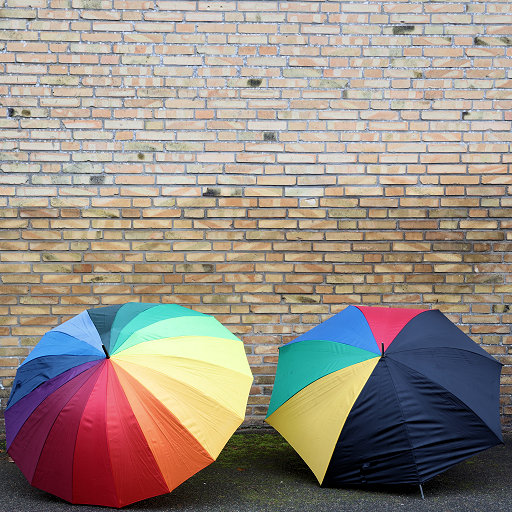 Zwei regenbogenfarbige Schirme vor einer Backsteinmauer