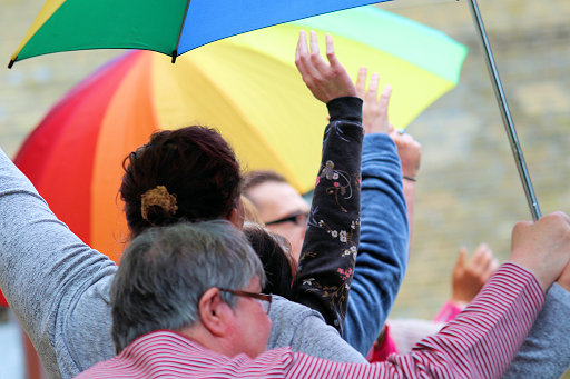 Winkende Menschen unter einem regenbogenfarbigen Schirm